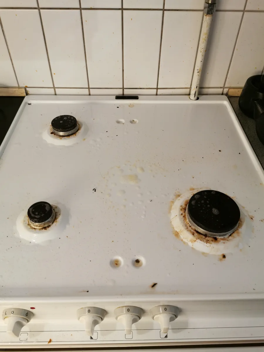 Hvidt emaljekomfur med indbrændte gule ringe omkring gasblusene før rengøring